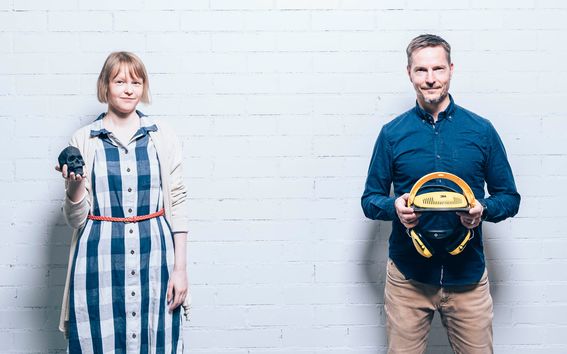 Yhteiskuvassa Juudit Ottelin ja Matti Kuittinen seisovat vierekkäin ja katsovat kohti kameraa. Ottelinin kädessä on pieni musta 3d-tulostettu pääkallo, Kuittinen pitelee käsissään työmaakypärää, jossa on kuulosuojaimet.