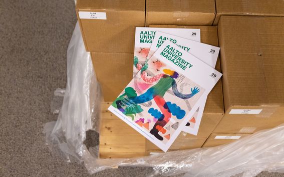 Kolme kappaletta uusinta Magazinea kuvattuna kirjapainosta tulleiden ruskeiden pahvilaatikoin päällä, laatikoiden ympäriltä on poistettu pakkausmuoveja.