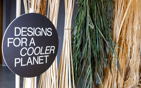 Photo of round black sign with white letters "Designs for a cooler planet" with dried reeds and grasses