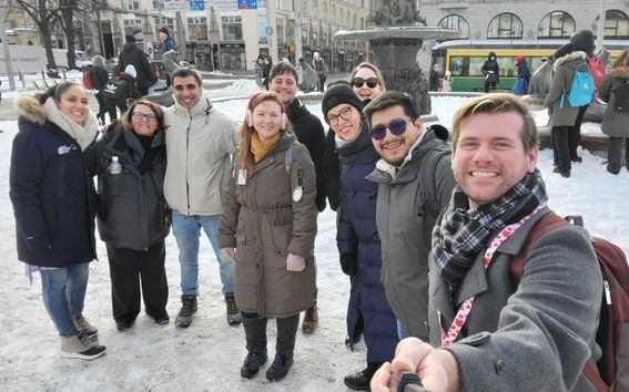 A group oicture taken with a selfie stick of a group of smiling Summer School students on the Market Squre in Helsinki.