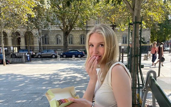 Kuvassa on kesä, ja Karla Helenius istuu puiston penkillä syömässä pieniä leivoksia. 