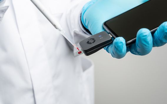 Valkoinen laboratoriotakki sekä analyysityökalu, jolla voidaan mitata veripisarasta särkylääkkeen pitoisuus.