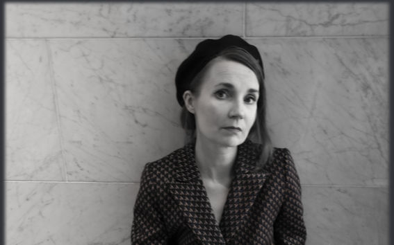 Mustavalkokuvassa nainen baskeri päässä istuu lattialla