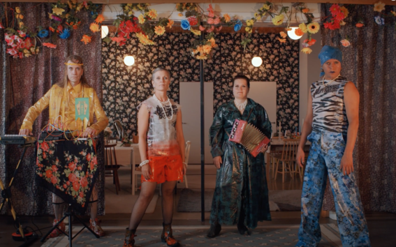 four band members posing on a small stage in colourful and shiny clothes