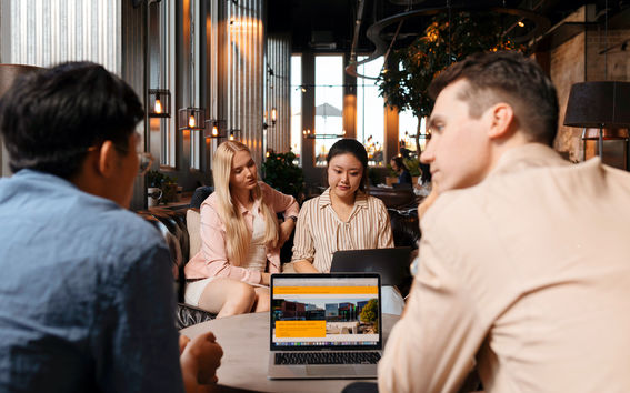Four students chatting and looking at a laptop in a cafeteria.