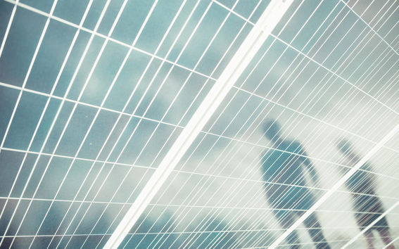 Reflections of two people on solar panels. Light blue sky is reflected on the background.
