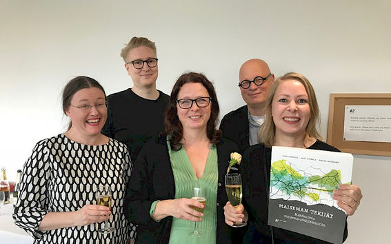 Maiseman tekijät -kirjan työryhmä juhlatunnelmissa poseeraa kirja kädessään