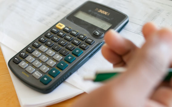 Kuvassa laskin ja käsi, joka pitelee vihreää mustekynää.