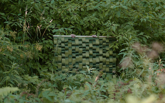 Two hands hold a green textiles surface surrounded by rich green nature all around  