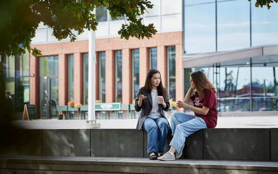 Two Aalto University students sitting under a big oak, drinking coffee and talking.