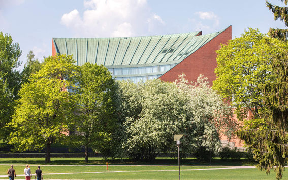 3 students walking with Otakaari 1 in the background in the summer