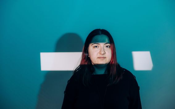 Ulviyya Quliyeva kuvattuna sinivihreää taustaa vasten siten, että hänen kasvoilleen osuu kirkas suorakaiteen muotoinen valkoinen valokeila.