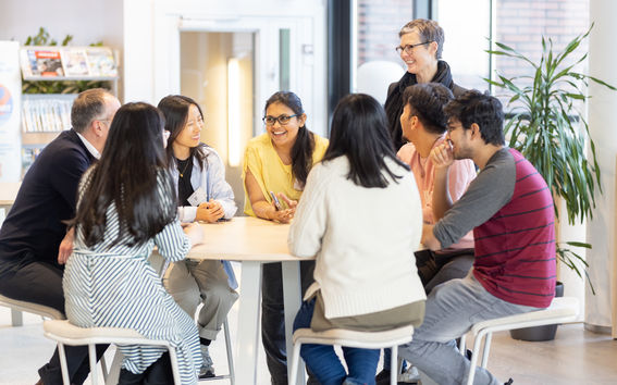Smiling people sitting and standing around a table.
