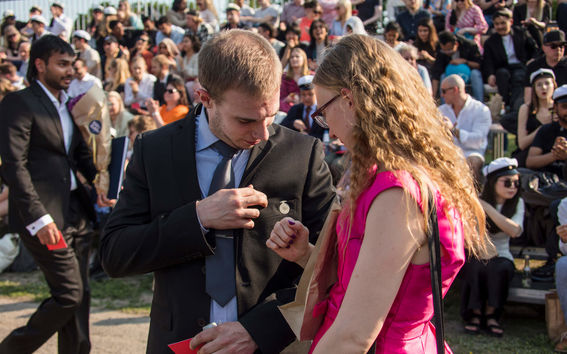 A new alumni putting on his graduation pin 