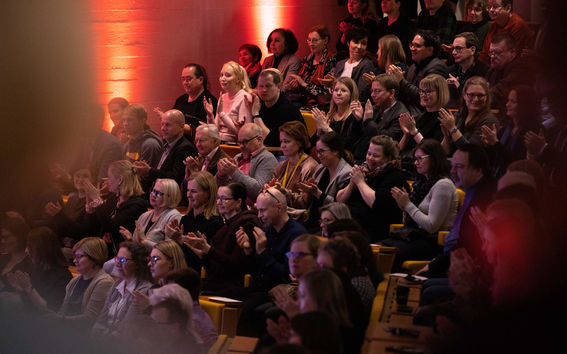 Hymyileviä ihmisiä aplodeeraamassa auditoriossa.