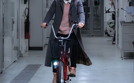 Professor Tiina Nypelö smiling and riding a red bicycle inside of a research facility