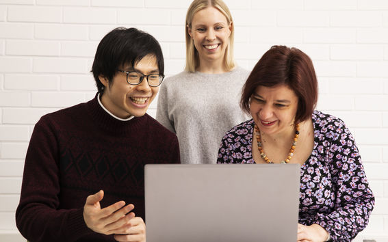 Kolme ihmistä katsoo jotain kannettavan tietokoneen näytöltä hymyillen.