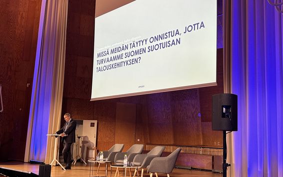 Kuvassa näkyy professori Teemu Malmi Aallon Töölön kampuksen juhlasalin lavalla pitämässä avauspuheenvuoroa Taloudenpuolustuskurssilla 2023. 