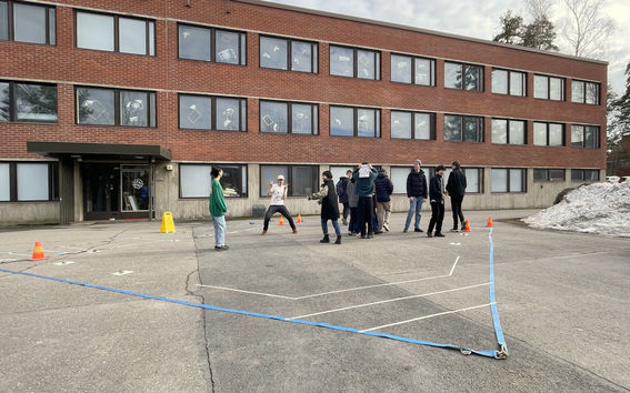 Students walking around the mockup of the stage layout, made with tape in a parking lot