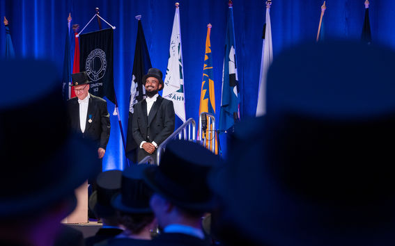 Kaksi mieshenkilöä juhlapuvuissa kiltalippujen edessä