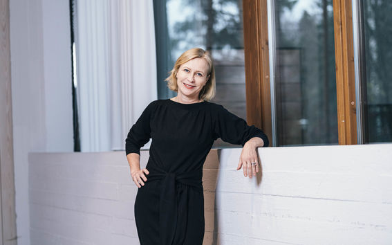 Nainen mustassa asussa nojaa vaaleaa seinää vasten