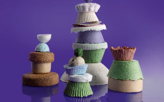 Eri muotoisia ja värisiä materiaalinäytteitä pinottuina neljälksi torniksi. Violetti tausta.