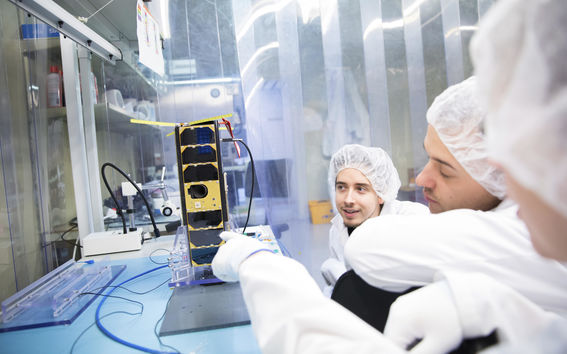 Ihmiset tutkivat pöydällä olevaa satelliittia.