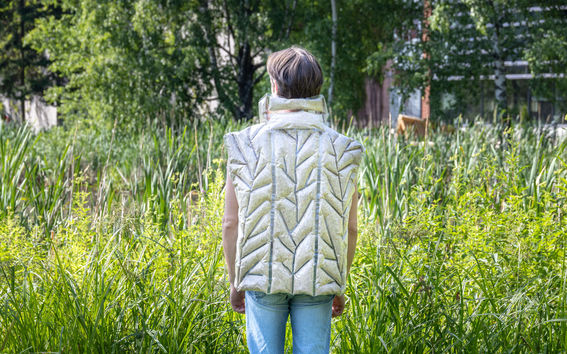 A person standing in front of a meadow, wearing a beige vest.