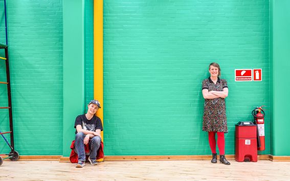 Jaana Vapaavuori ja Anne Louise Bang kuvattuna kirkkaanvihreän tiiliseinän edessä.