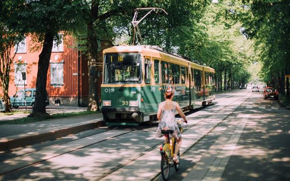 A Helsinki tram in a boulevard and a biker riding alongside it.