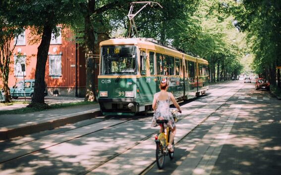A Helsinki tram in a boulevard and a biker riding alongside it.