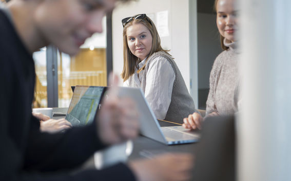 People in a meeting room working on laptops. One person gives a thumbs up.