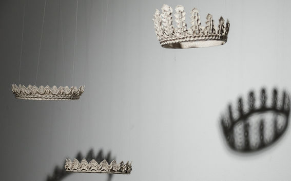 Three suspended crowns casting shadows on a grey wall.