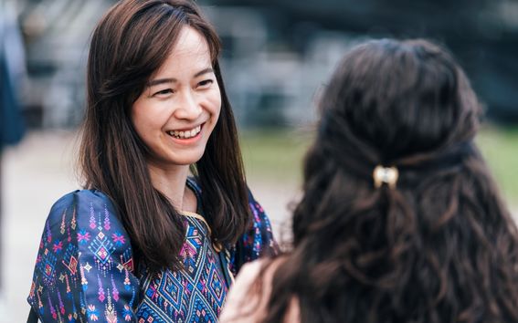 Two women with long hair talking and smiling; one wears a patterned blue top, the other has a hair clip.