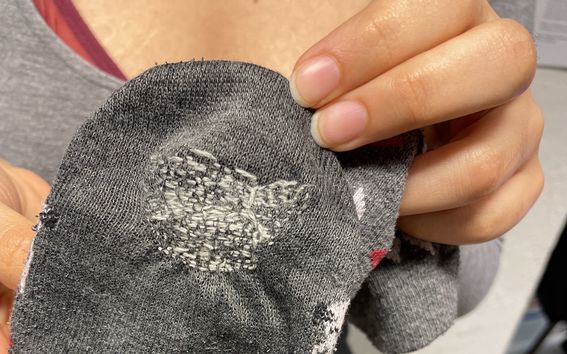 Student showing their mended sock in a mending workshop at Space 21.