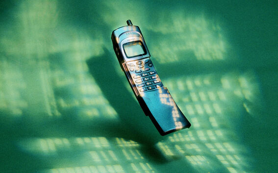Vanhanaikainen matkapuhelin, jossa on sisään vedettävä antenni, vihreällä taustalla ja hajavalokuvioilla.