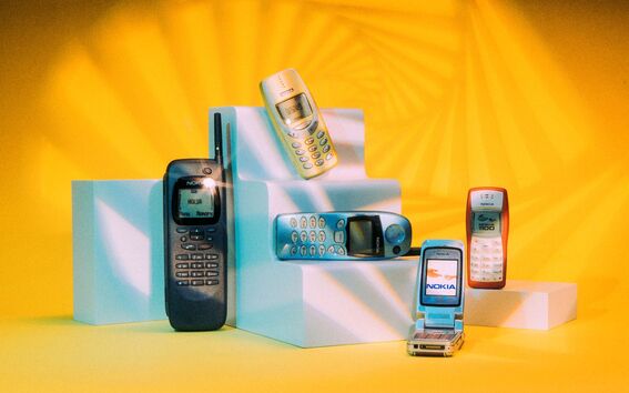 Five vintage Nokia mobile phones on white pedestals with a yellow background and geometric light patterns.