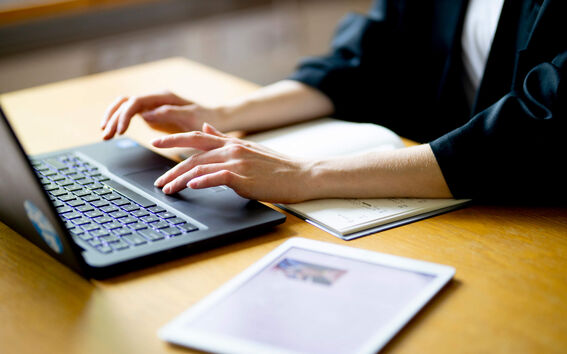 Person typing on a laptop with a notebook and tablet on the desk.