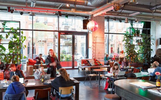 A trendy cafe with people working on laptops, chatting, and sitting on colourful furniture.