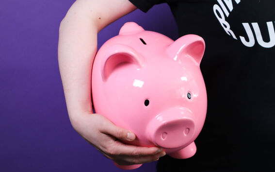 Person in black shirt holding a large pink piggy bank against a purple background.