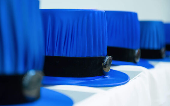 A row of blue academic doctoral hats with black bands and emblems displayed on a white surface.