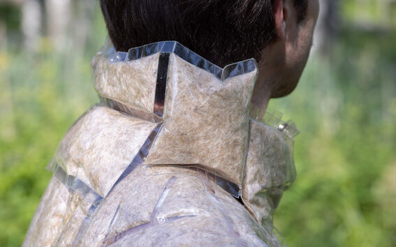 A person wearing a jacket made of clear plastic bags filled with brown fibrous material, seen from the side.