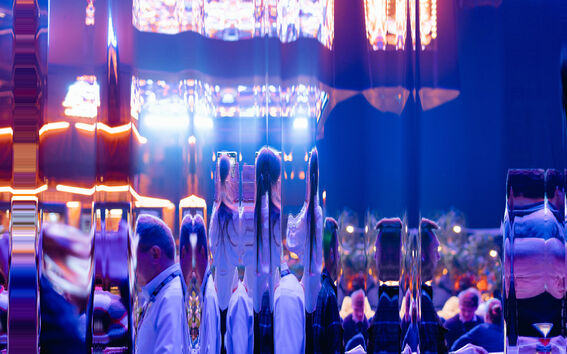 A reflective surface distorts the view of people dressed formally in a vibrant room with bright lights.