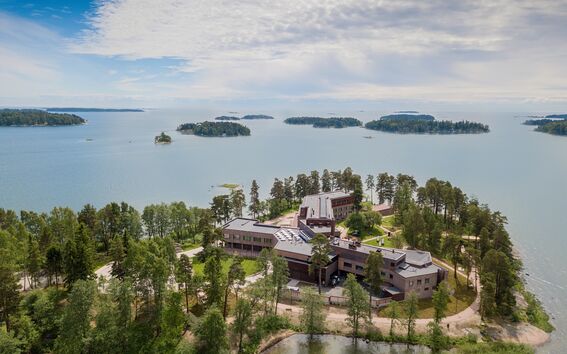 An aerial view of a complex of buildings on a forested peninsula surrounded by a lake with multiple small islands.