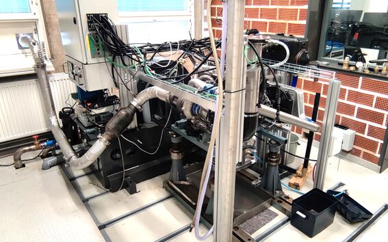 Yksityiskohtainen näkymä teollisuuskoneesta, jossa on useita johtoja ja putkia huoneessa, jossa on tiiliseinät ja ikkunat.