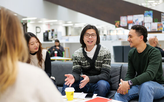 A group of people having a discussion in a modern indoor setting with notebooks and a yellow coffee cup on the table.