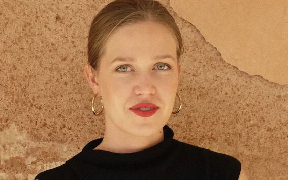 Person wearing a sleeveless black top with crossed arms in front of a textured beige wall.