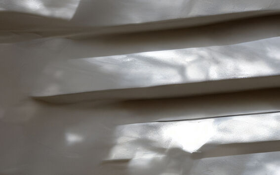 Lähikuva valkoisesta kierreportaasta tai sisäseinärakennelmasta, jonka pinnalle luonnonvalo luo abstrakteja kuvioita ja varjoja.