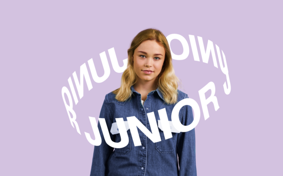 Nainen farkkupaidassa ja -housuissa purppurataustalla sanojen 'JUNIOR' ympäröidessä häntä.