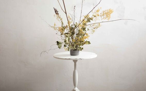 A white side table with a floral arrangement made out of dry flowers sits against a textured wall and patterned floor.
